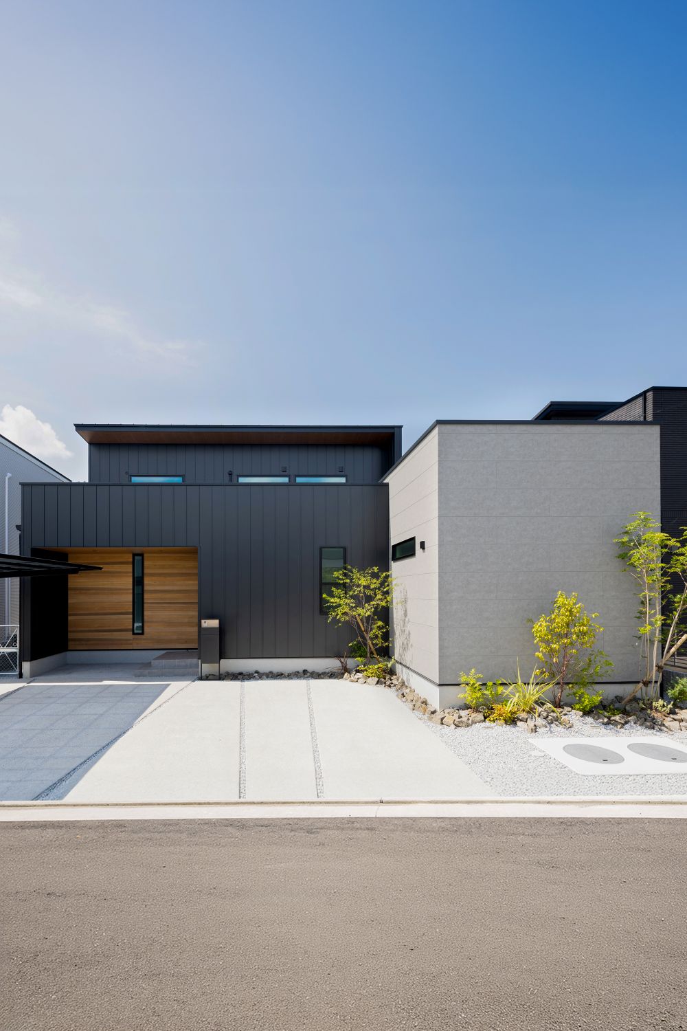 黒ととライトグレーの外壁に木目の玄関まわりを組み合わせたモダンな二階建て住宅